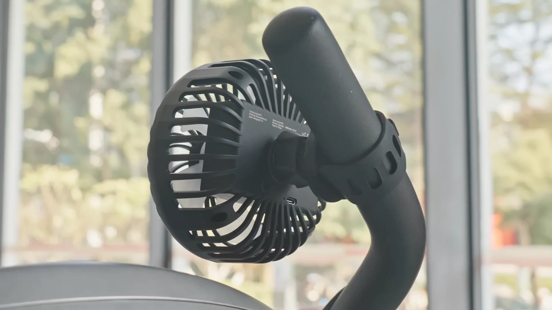 Rechargeable A2C fan strapped to a handlebar next to a window