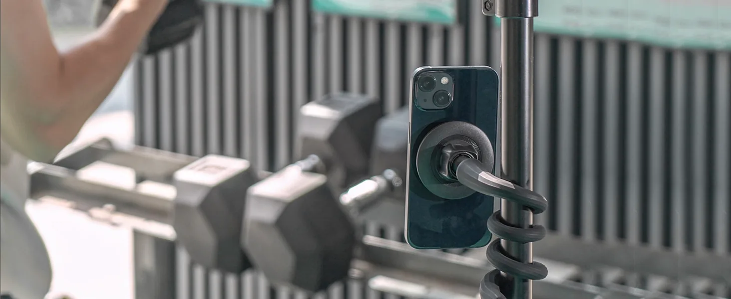 Phone held on a magnetic gym mount beside a dumbbell rack
